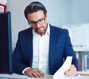 Business, man and computer with document in office as receptionist, financial schedule and email feedback. Administrator, legal paperwork and reading for project report, budget and policy information.